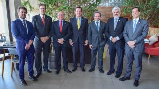 Imagem mostra sete homens em pé olhando para a câmera. Todos estão de traje social e gravata. O conselheiro Adircélio de Moraes Ferreira Júnior (TCE/SC) está ao centro, de traje escuro, camisa azul e gravata amarela.